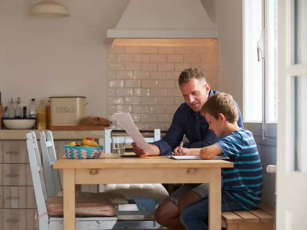 Support worker sat at a table with a young person helping with their work