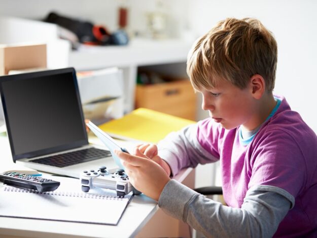 Young person on their phone and laptop in their bedroom