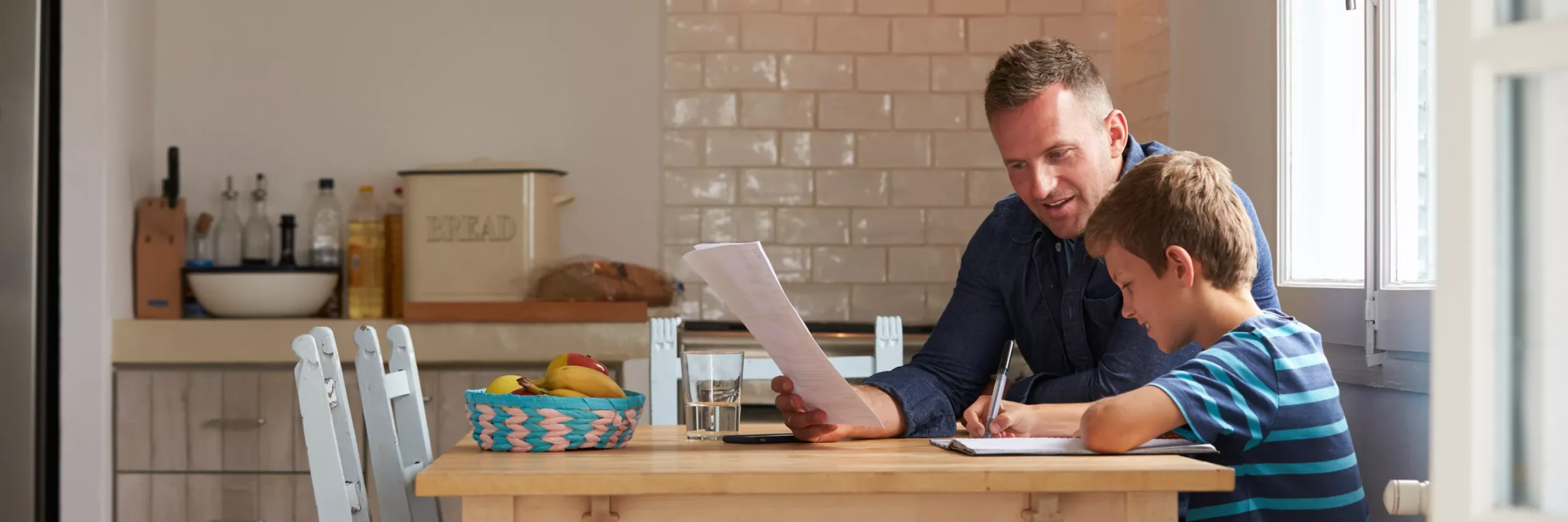 Support worker sat at a table with a young person helping with their work